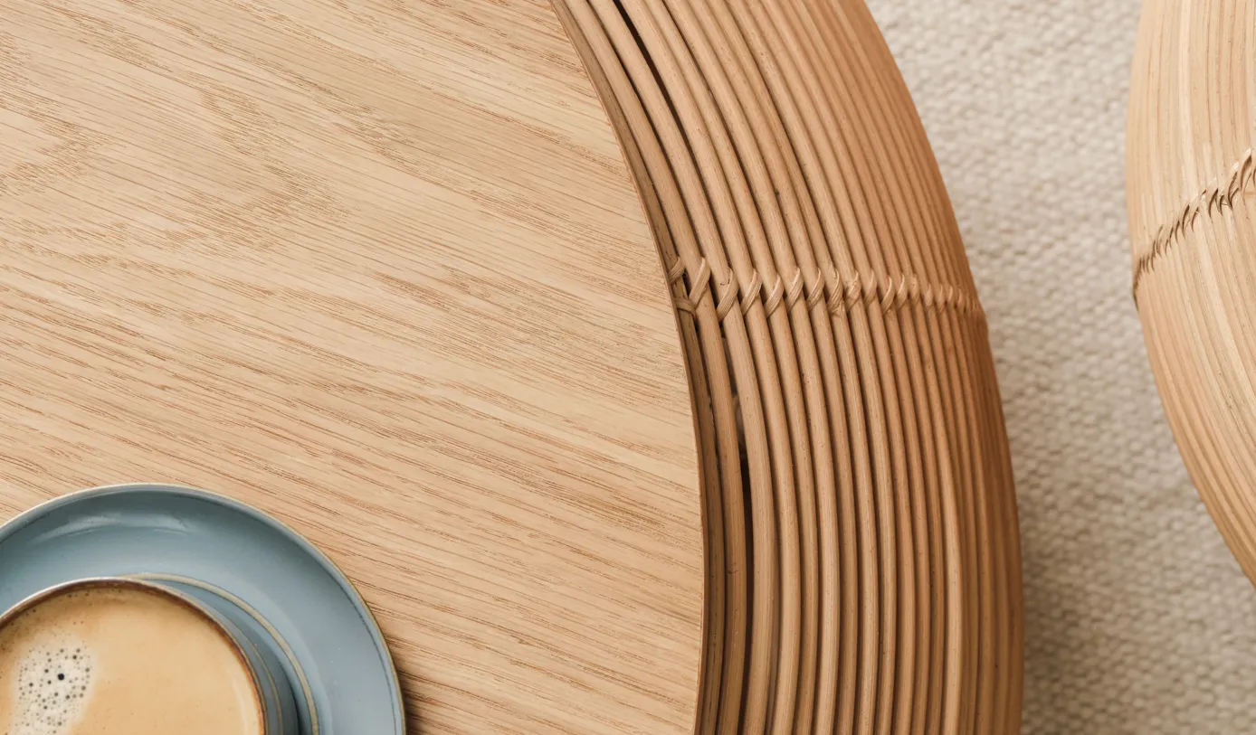Vivi coffee table by Vincent Sheppard in natural oak, with a finely crafted rattan frame and a blue cup of coffee on top, set on a neutral rug.